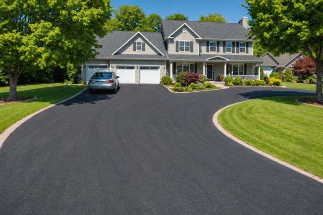 Freshly laid asphalt driveway with visible sealcoating, surrounded by lush green grass, under a clear sunny sky